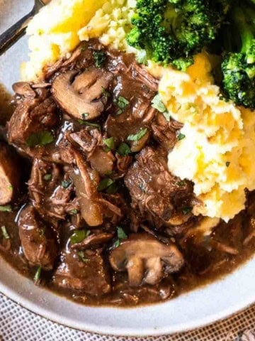 Slow cooker beef tips with gravy plated with mashed potatoes and broccoli.
