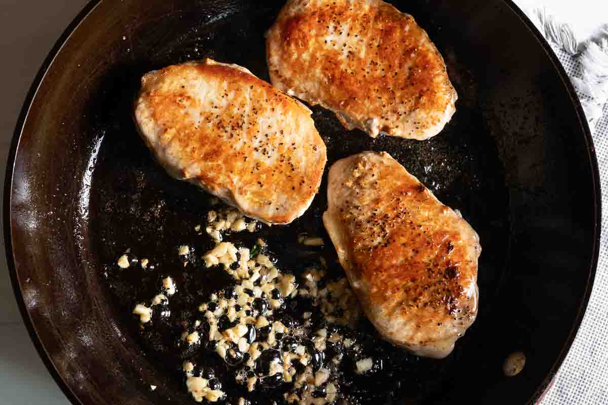 Seared pork chops in a skillet with honey garlic sauce.