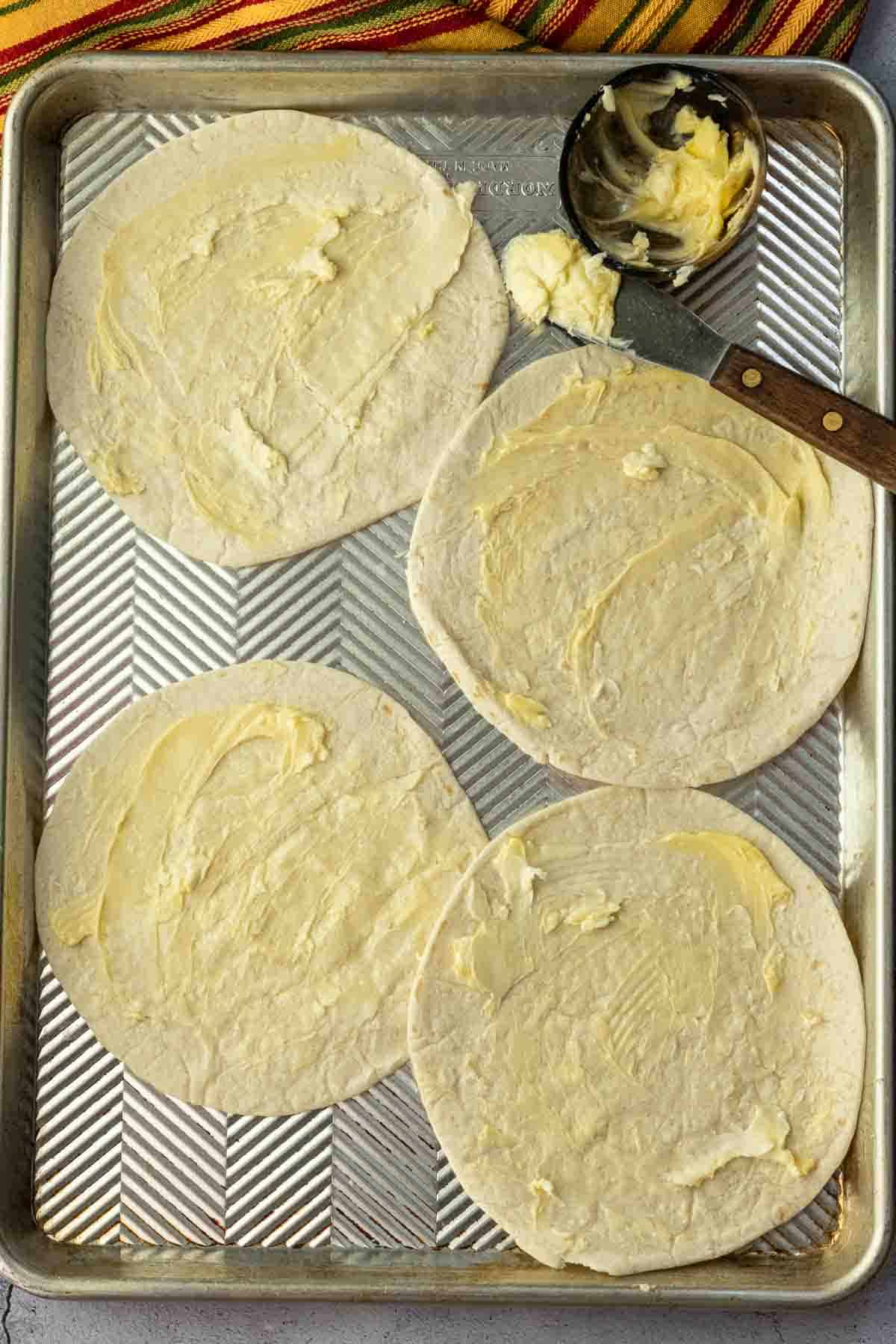 Buttering flour tortillas to make chicken bacon ranch quesadillas.
