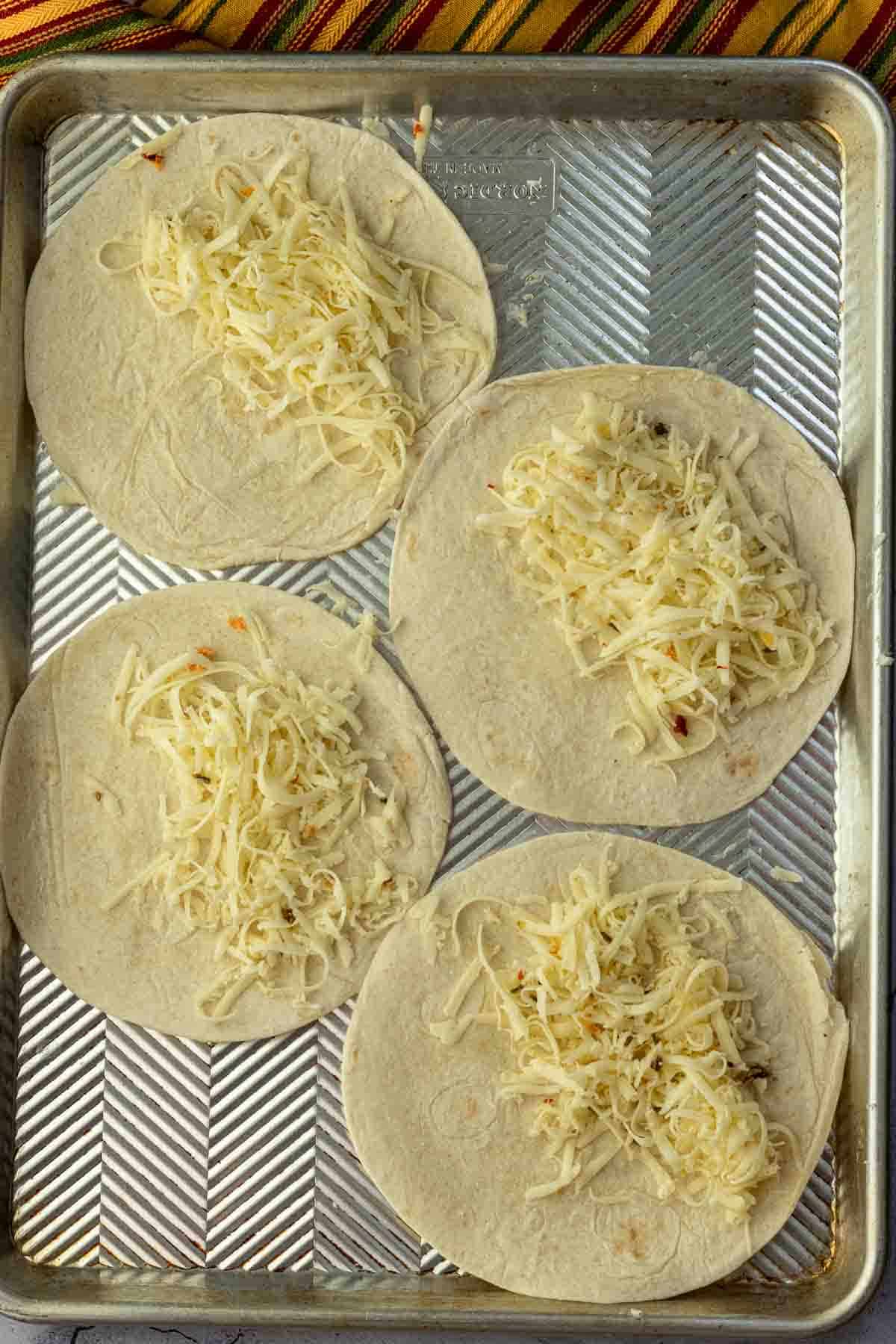 Adding cheese to flour tortillas to make chicken bacon ranch quesadillas.