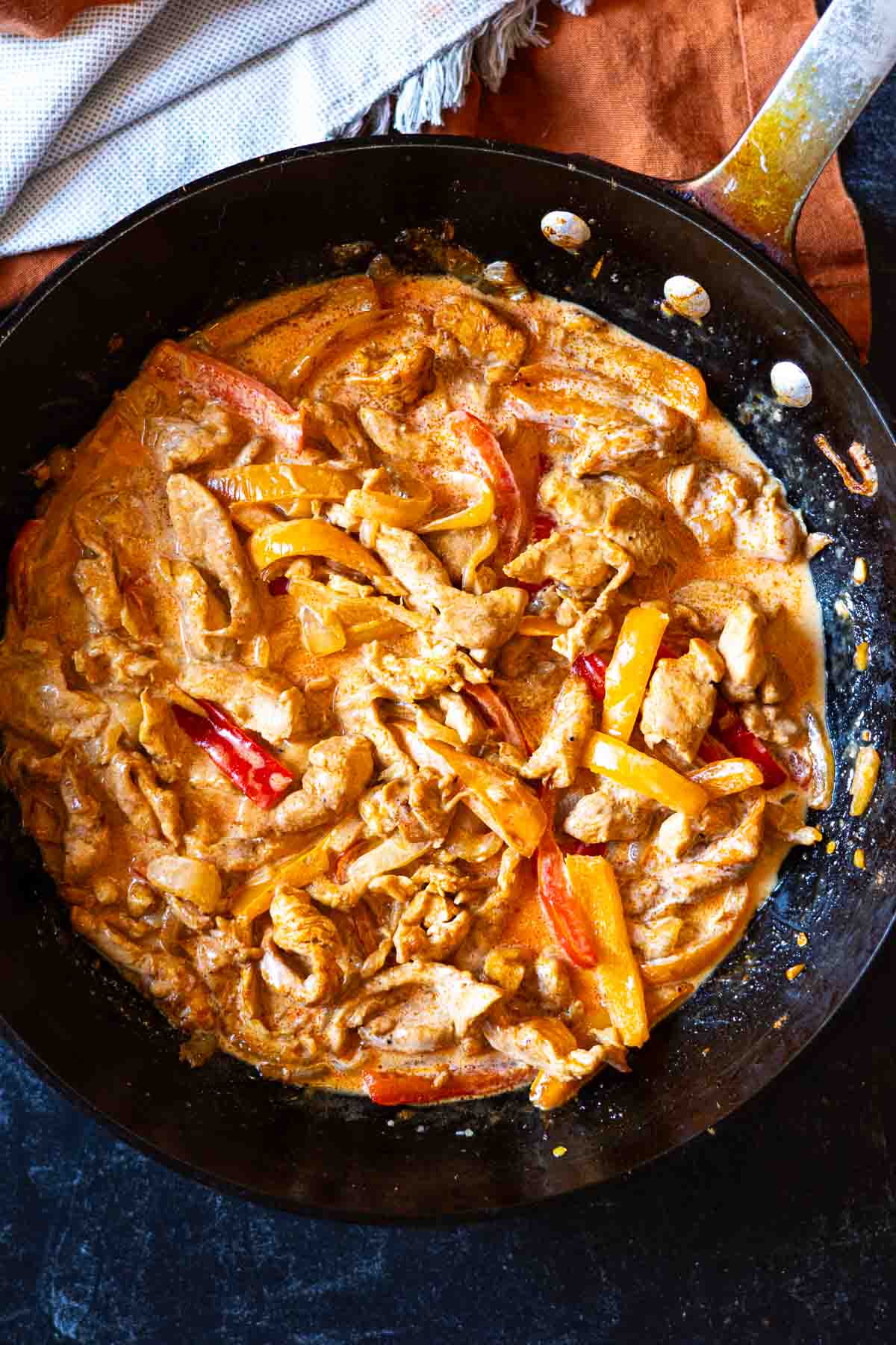 Adding cream and pasta to chicken and vegetables to make chicken fajita pasta.