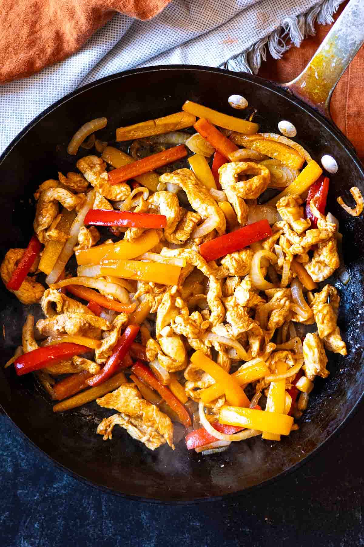 Cooking chicken and vegetables in a large skillet to make chicken fajita pasta.