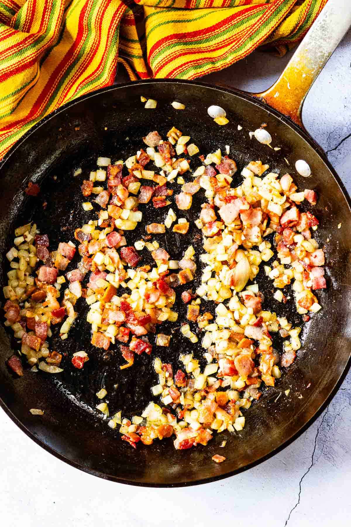 Cooking bacon, onions and garlic in a large fry pan to make bbq baked beans on the grill.