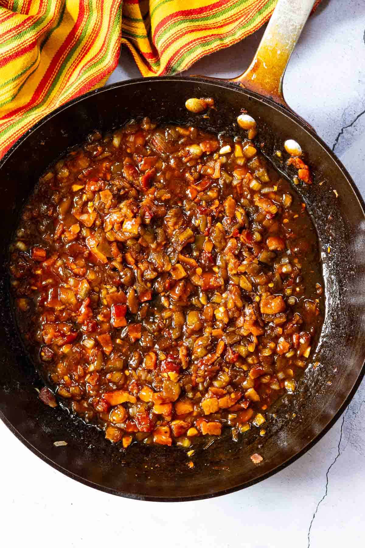 Adding sauce ingredients to skillet to make bbq baked beans on the grill.