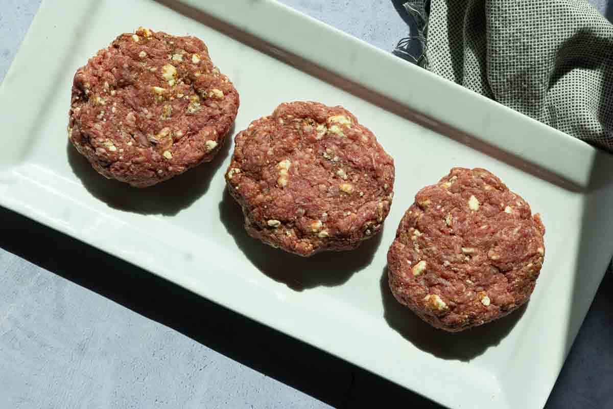 Three black and blue hamburger patties ready to grill.