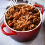 A red crock full of baked beans cooked on the grill.