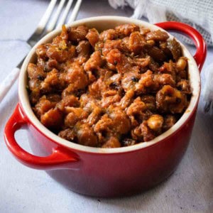 A red crock full of baked beans cooked on the grill.