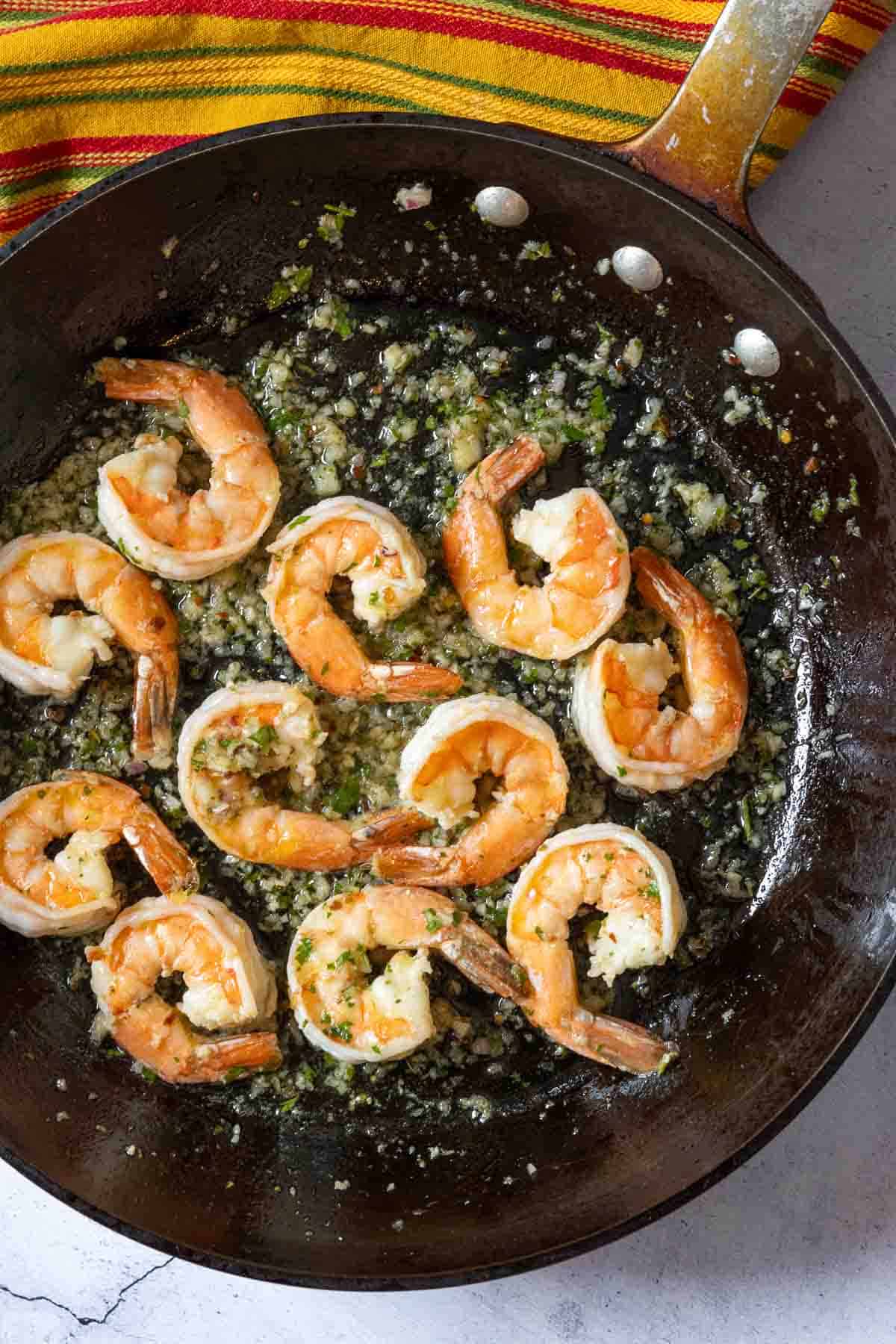 Adding chimichurri sauce to cooked shrimp in a skillet to make shrimp chimichurri.