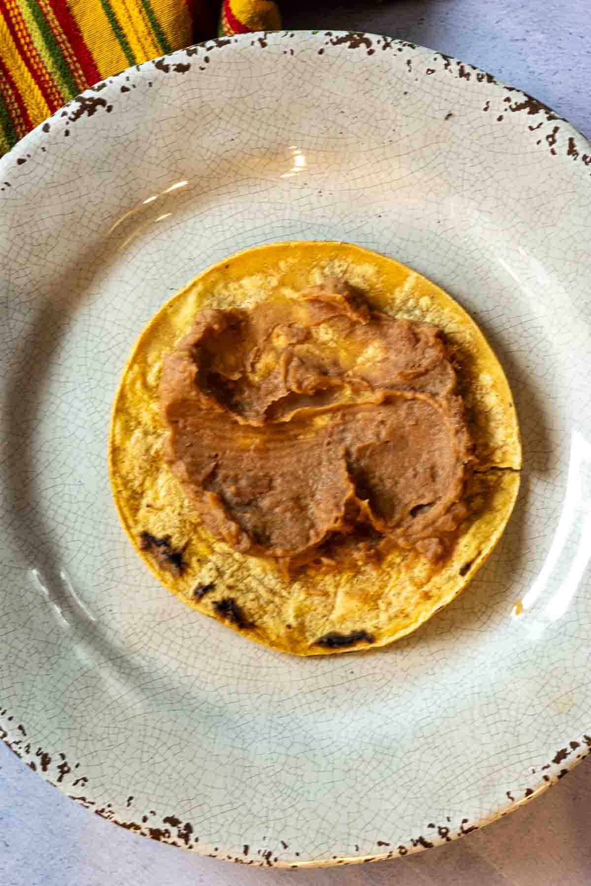 Smearing refried beans on a corn tortilla to make tortilla burgers.