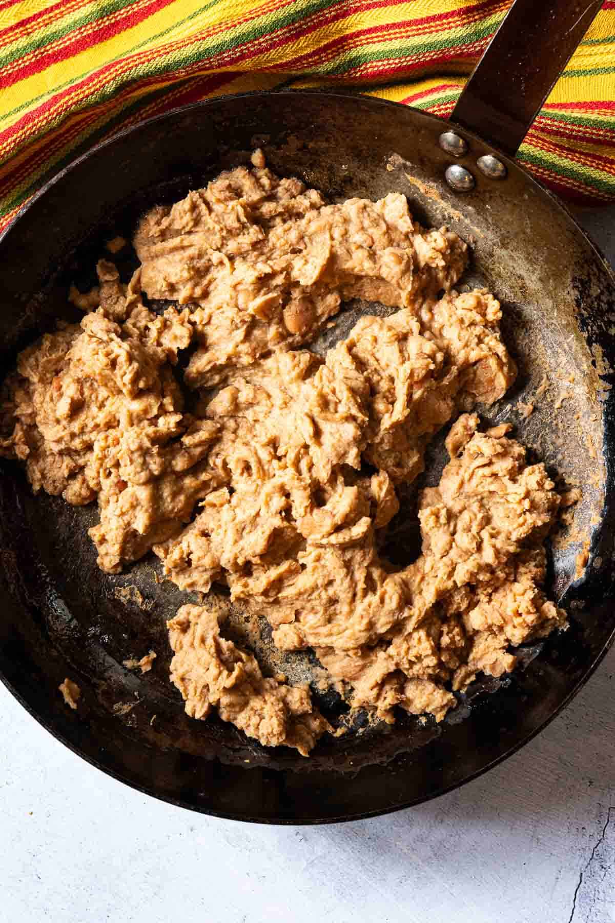 Heating up canned refried beans in a skillet to make tortilla burgers.