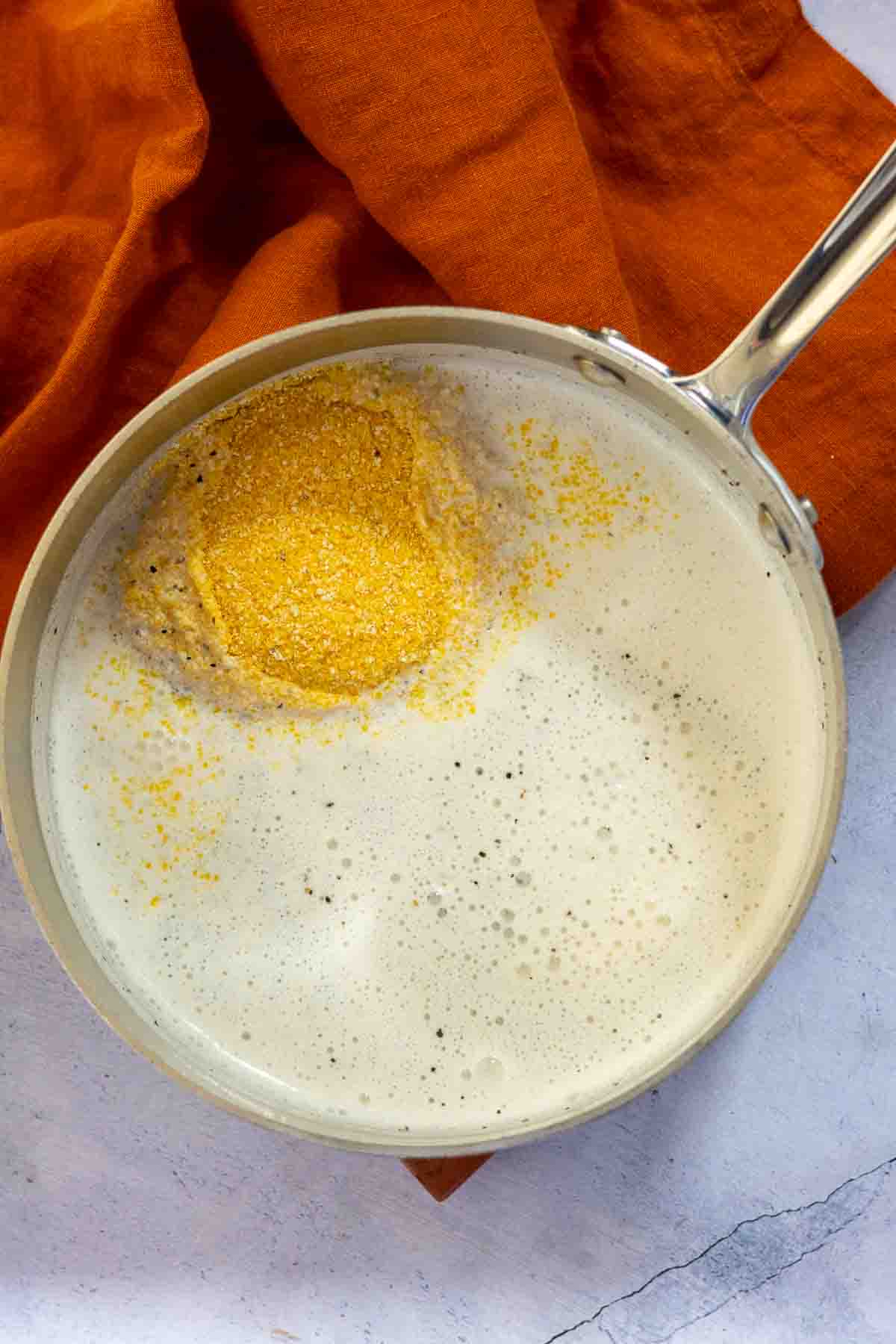 Adding polenta to half and half to make creamy polenta and shrimp.