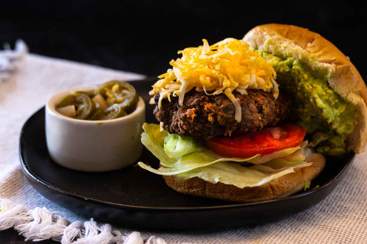 Taco burger topped with shredded cheddar cheese, and topped with smashed avocado.