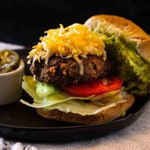Taco burger on a sesame seed bun topped with shredded cheese and smashed avocado.
