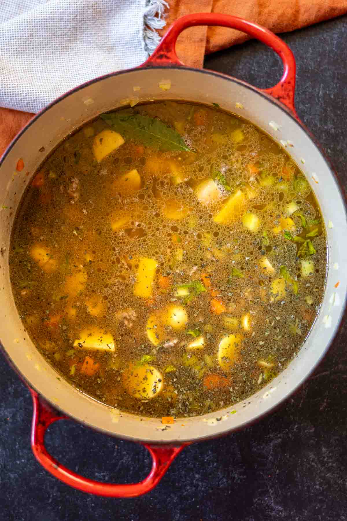 Adding beef broth and spices to soup ingredients to make hamburger potato soup.