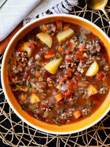 Hamburger potato soup served in an orange bowl.