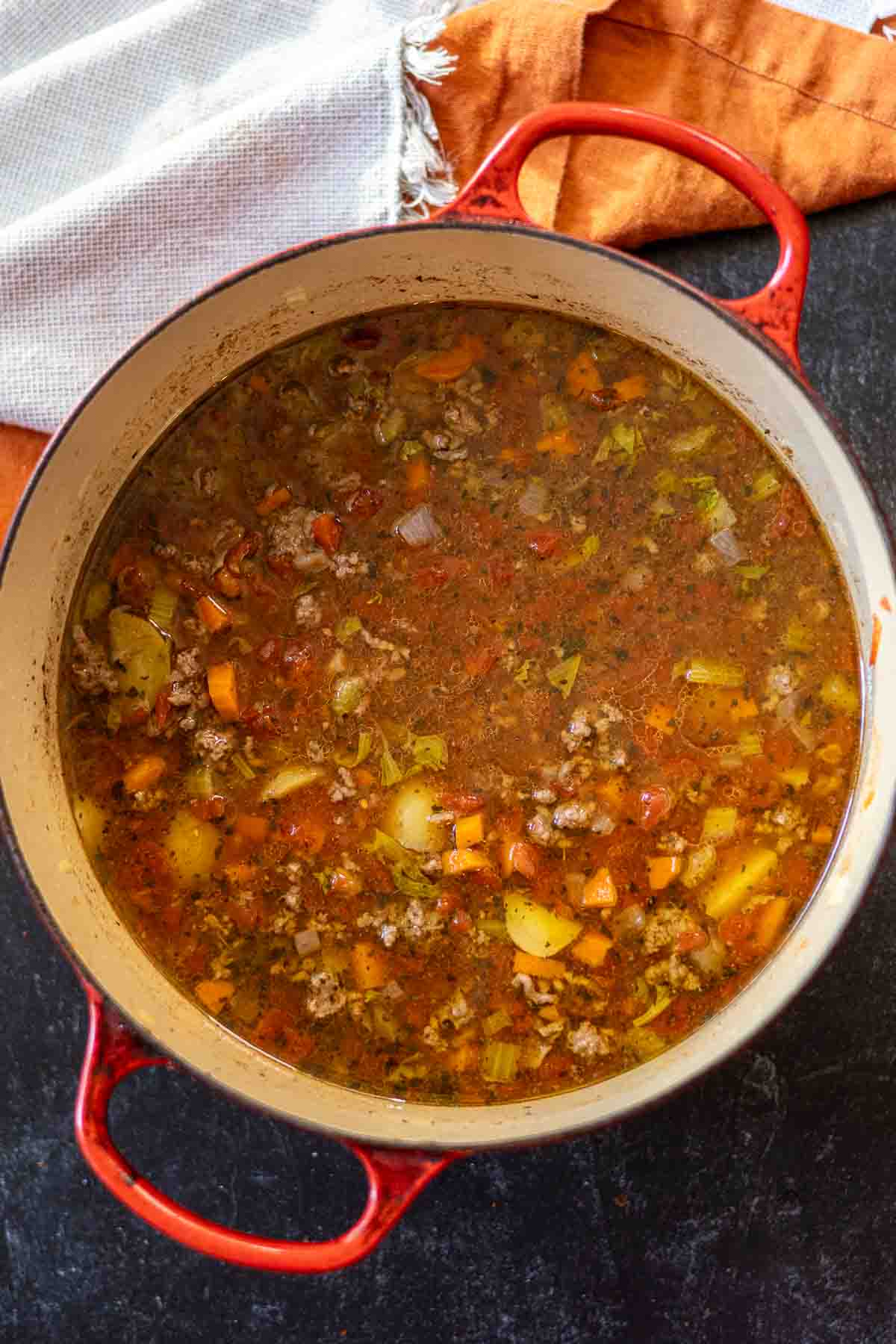 Adding tomatoes to soup ingredients to make hamburger potato soup.