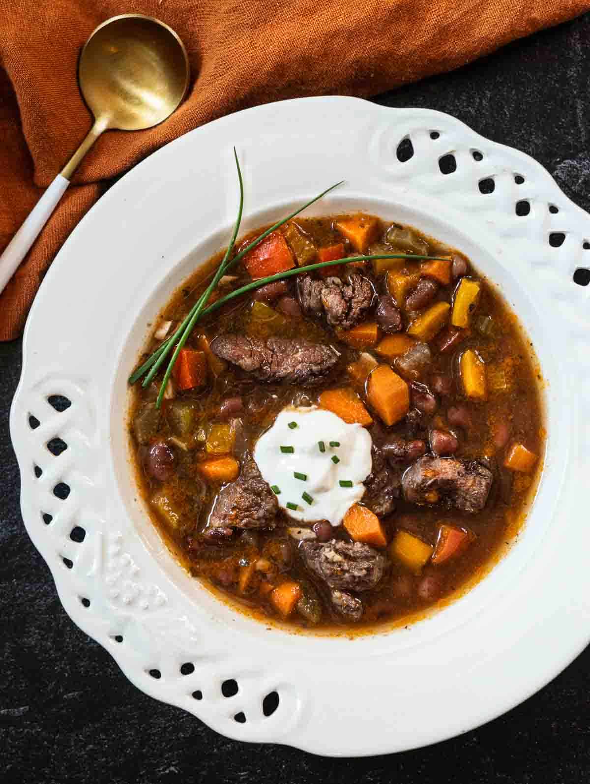 Bean and beef soup served in a shallow white bowl, topped with a spoonful of sour cream.
