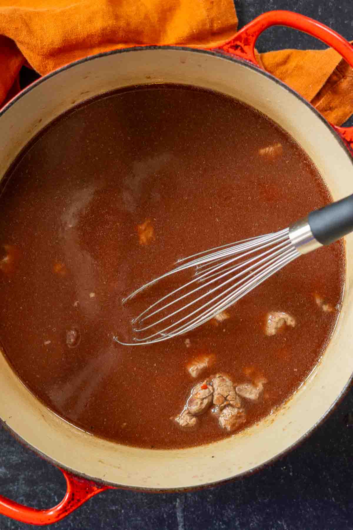 Adding red wine and beef stock to vegetables to make bean and beef soup.