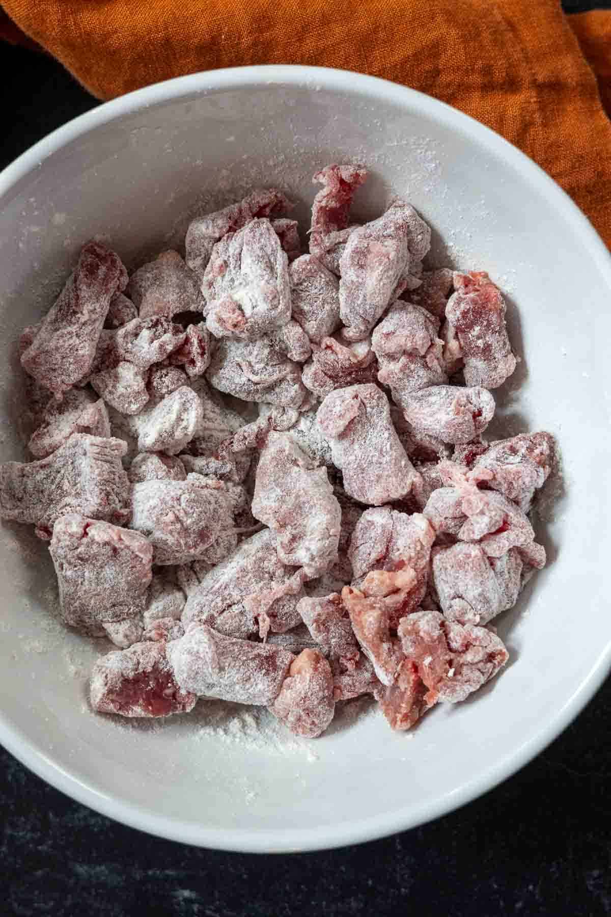 Flouring beef pieces to sear, to make bean and beef soup.