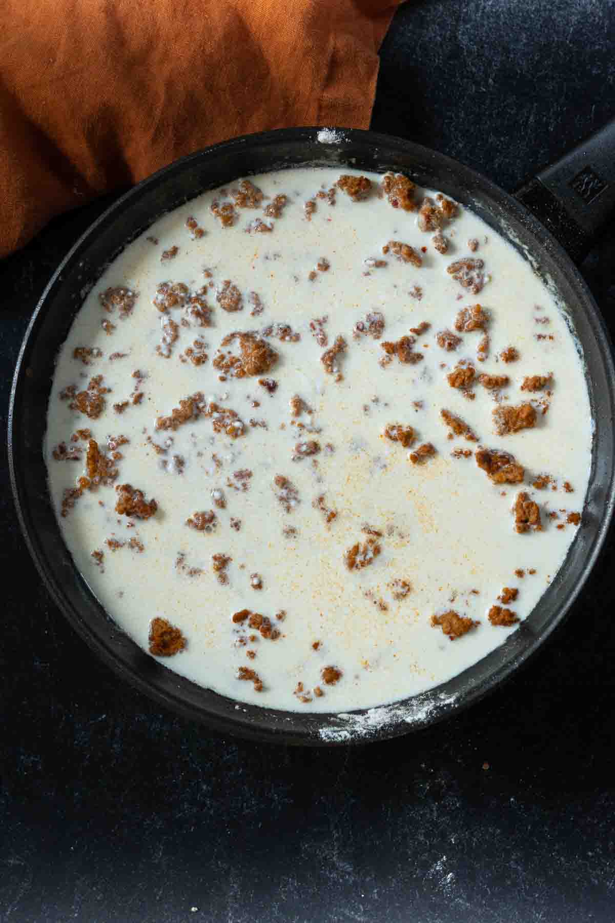 Adding milk to sausage to make chorizo gravy in a skillet.