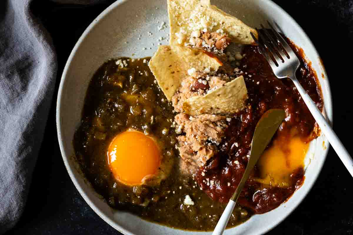 Huevos Divorciados on a plate with refried beans and corn chips.