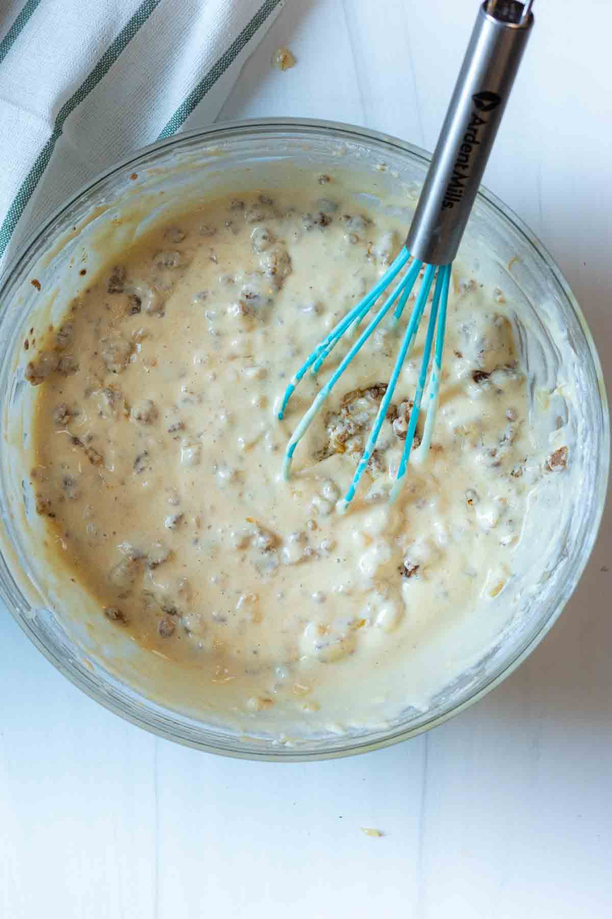 Adding cooked sausage to pancake batter to make sausage pancakes.