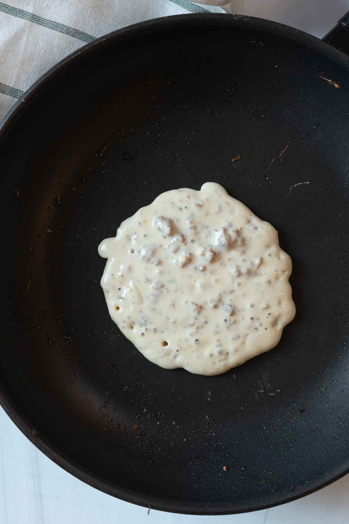 Cooking pancakes in a skillet to make sausage pancakes.