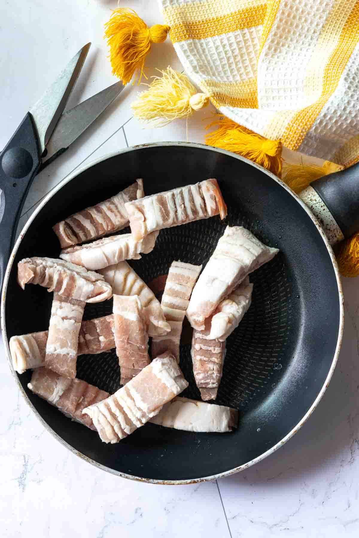 Cutting raw bacon into pieces to fry and make cottage cheese egg bites.