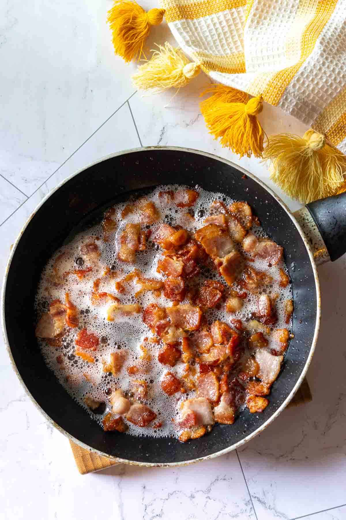Cooking bacon bits in a fry pan to make cottage cheese egg bites.