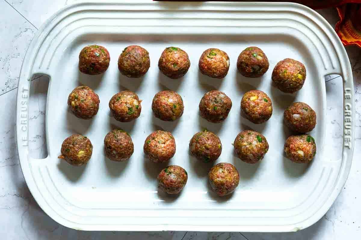 Uncooked bison meatballs on a white platter.