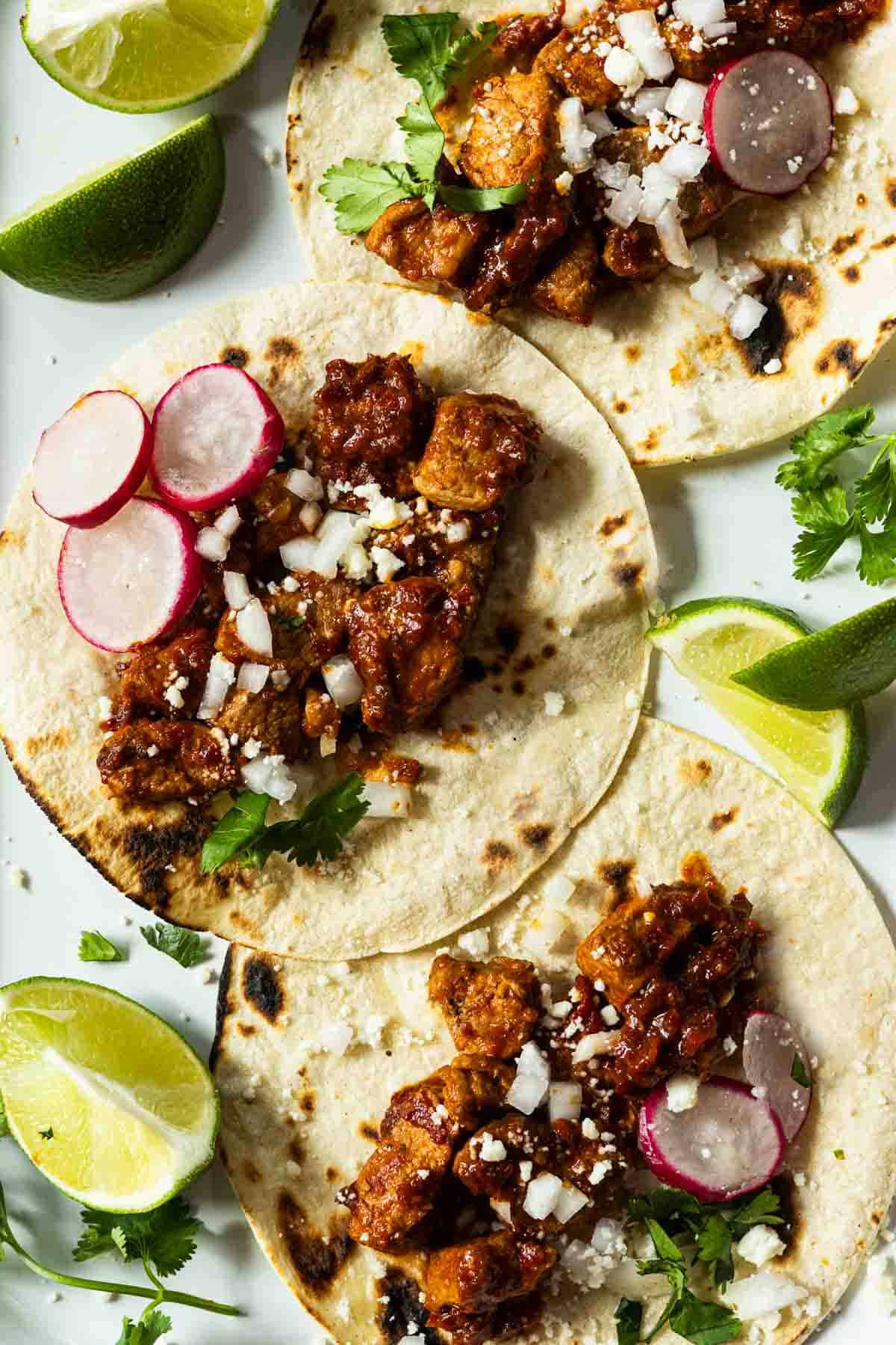 Three Orange Guajillo Pork Tenderloin Tacos garnished with onions and lime.