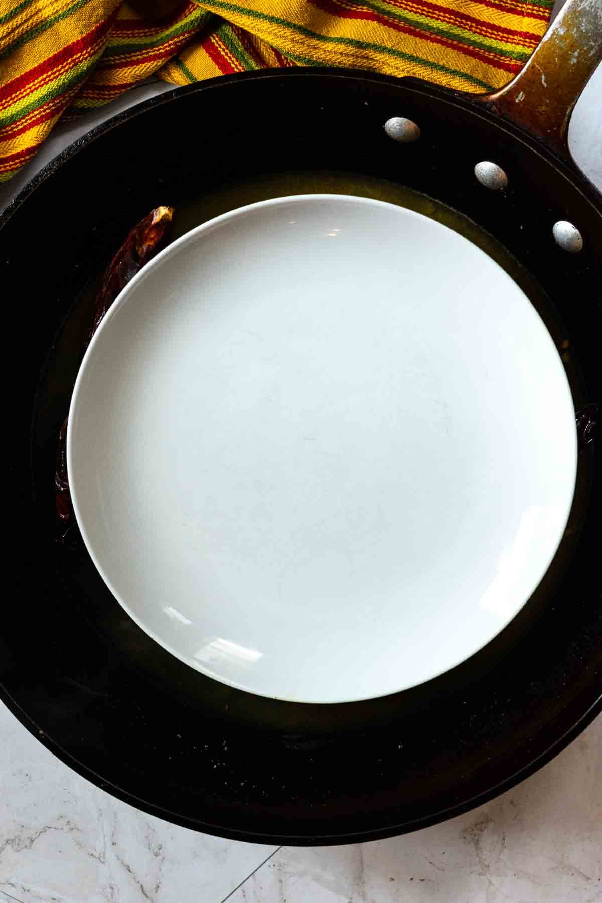 Placing a plate over guajillo chiles to keep them submerged in liquid.