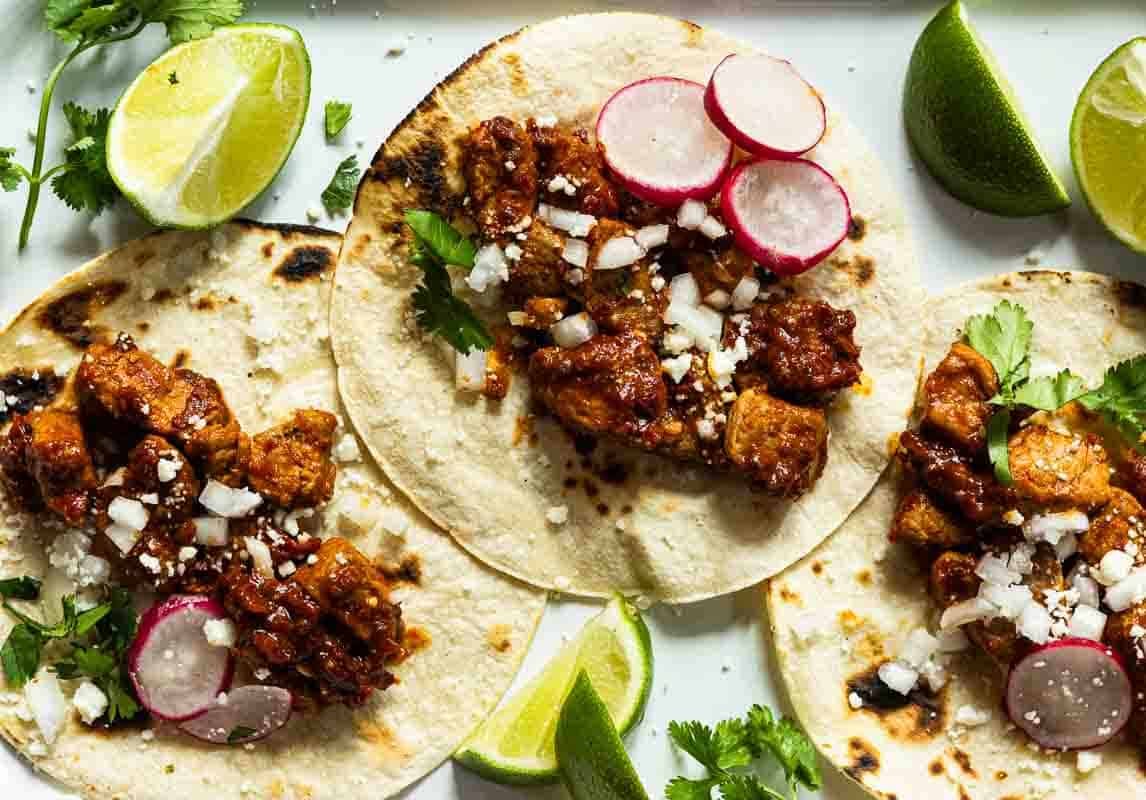 Pork Tenderloin tacos in chile guajillo sauce with toppings.