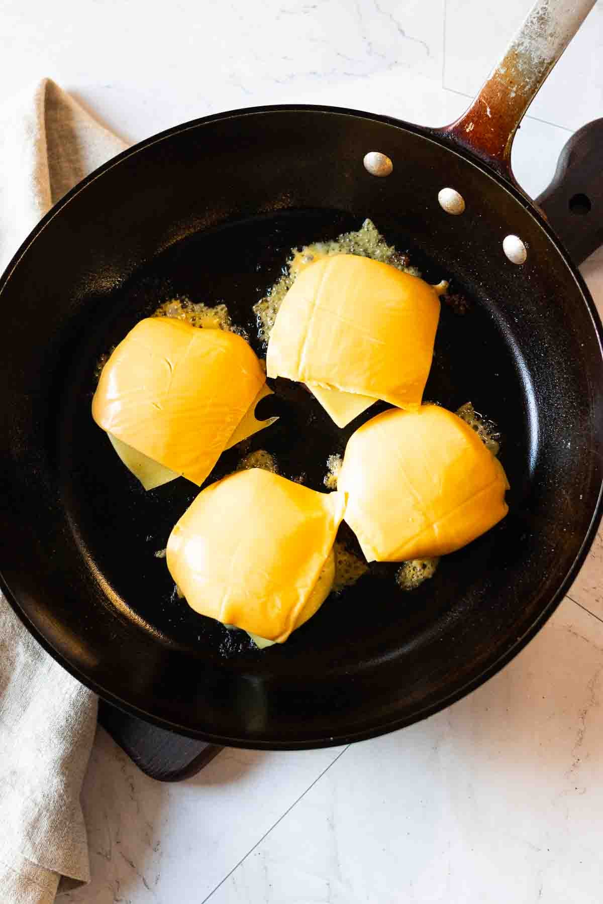 Adding cheese to pan seared burger patties.