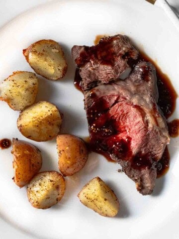 A slice of chuck eye roast on a plate served with roasted potatoes.