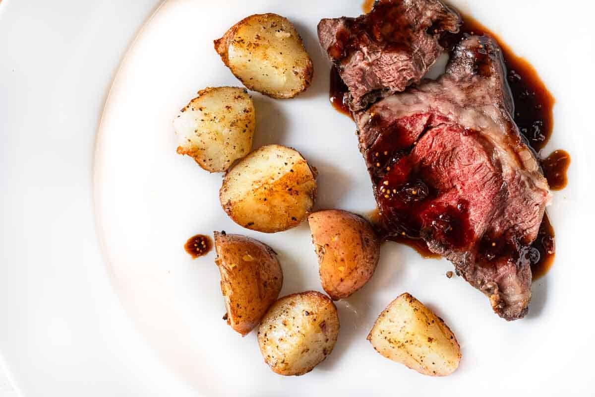 A slice of chuck eye roast served with fried potatoes and balsamic fig sauce.