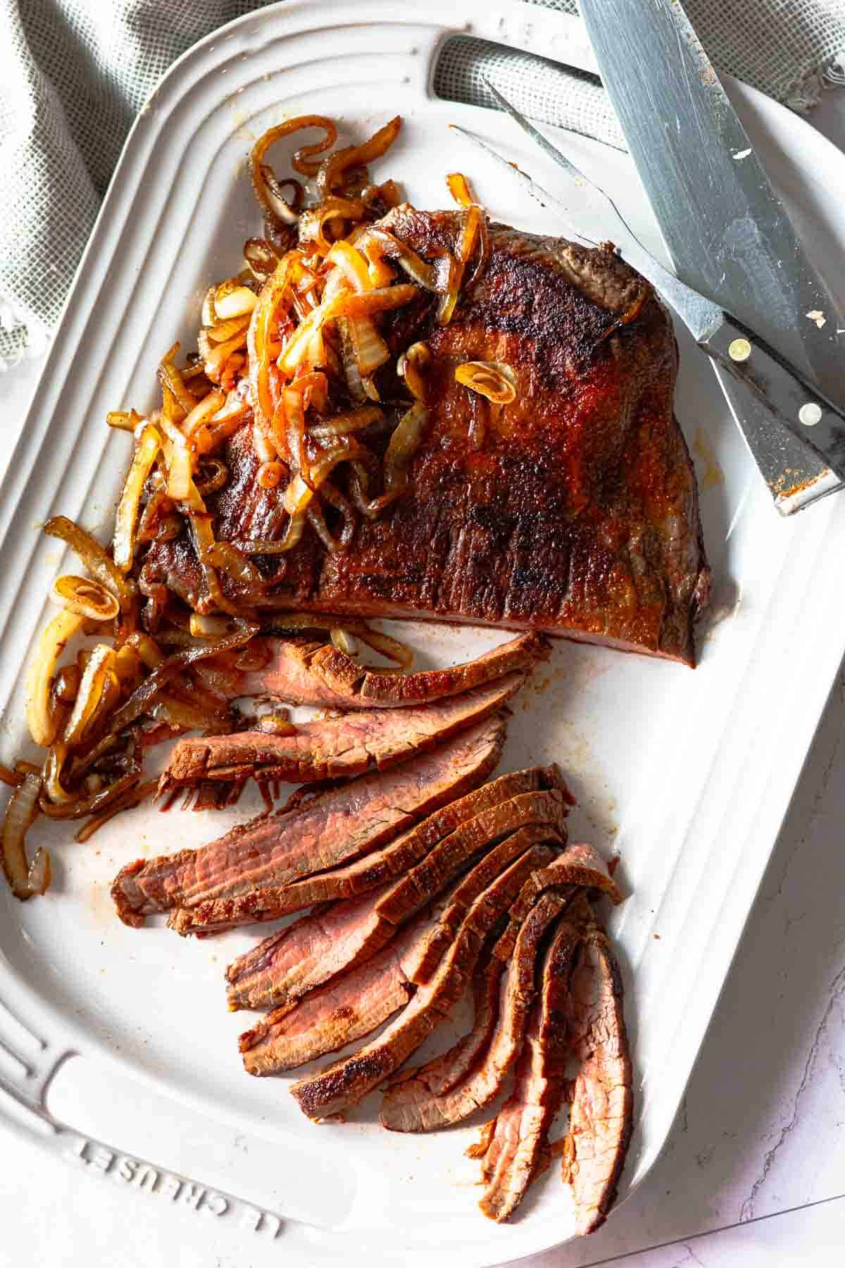 Pan seared flank steak sliced and served on a white platter with charred onions.