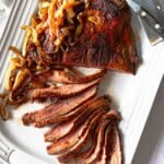 Sliced cast iron flank steak served on a white platter with charred onions.