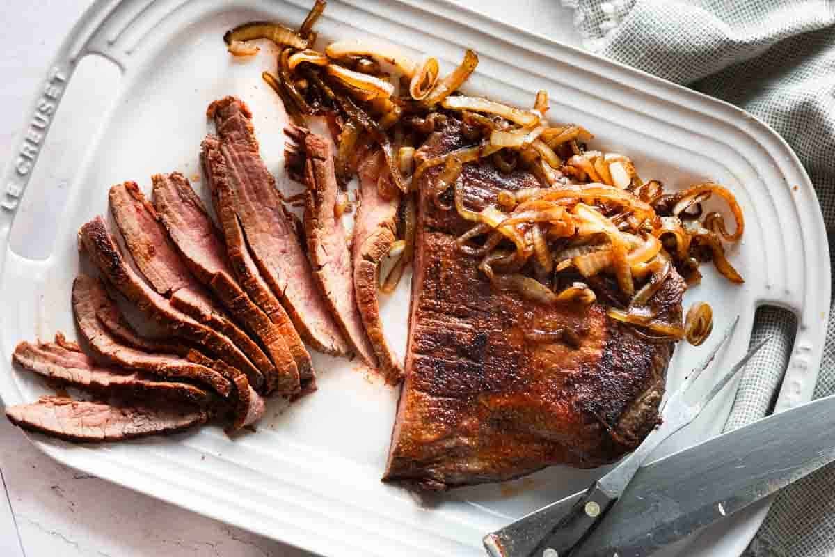 Cast Iron Flank Steak served on a white platter with charred onions.