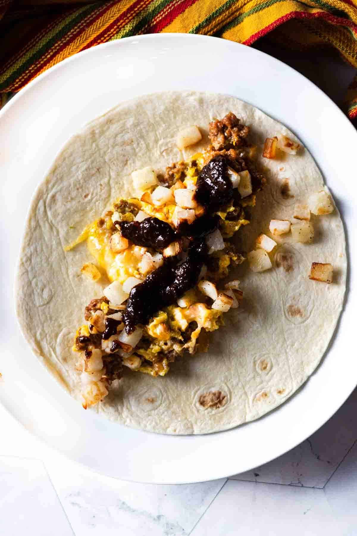 Step 6: Adding red chile sauce to a chorizo breakfast burrito.