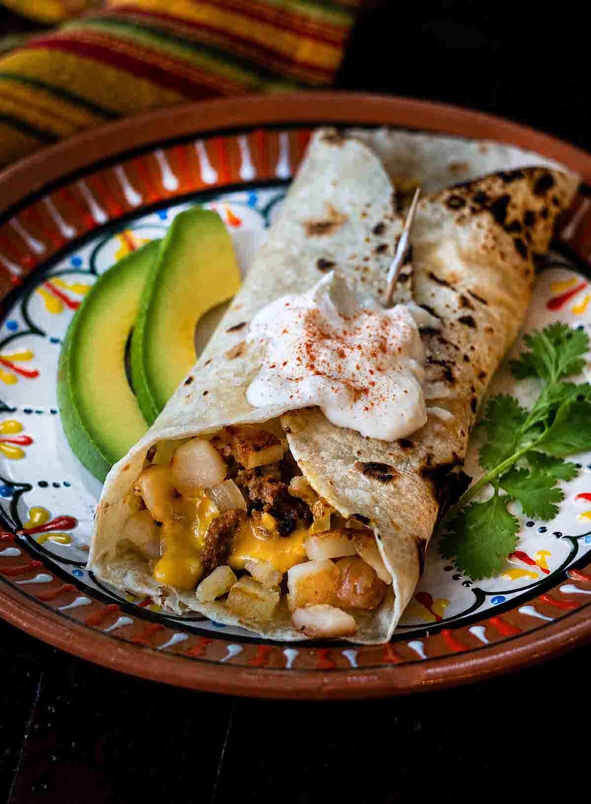 Breakfast chorizo burrito with potatoes and eggs. Garnished with avocado slices and cilantro.