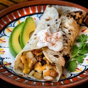 Chorizo breakfast burrito served with sliced avocado and sour cream.