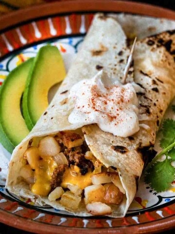 Chorizo breakfast burrito served with sliced avocado and sour cream.